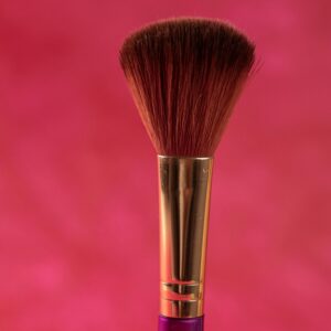 Detailed close-up of a makeup brush on a vibrant pink background, perfect for beauty and cosmetics themes.