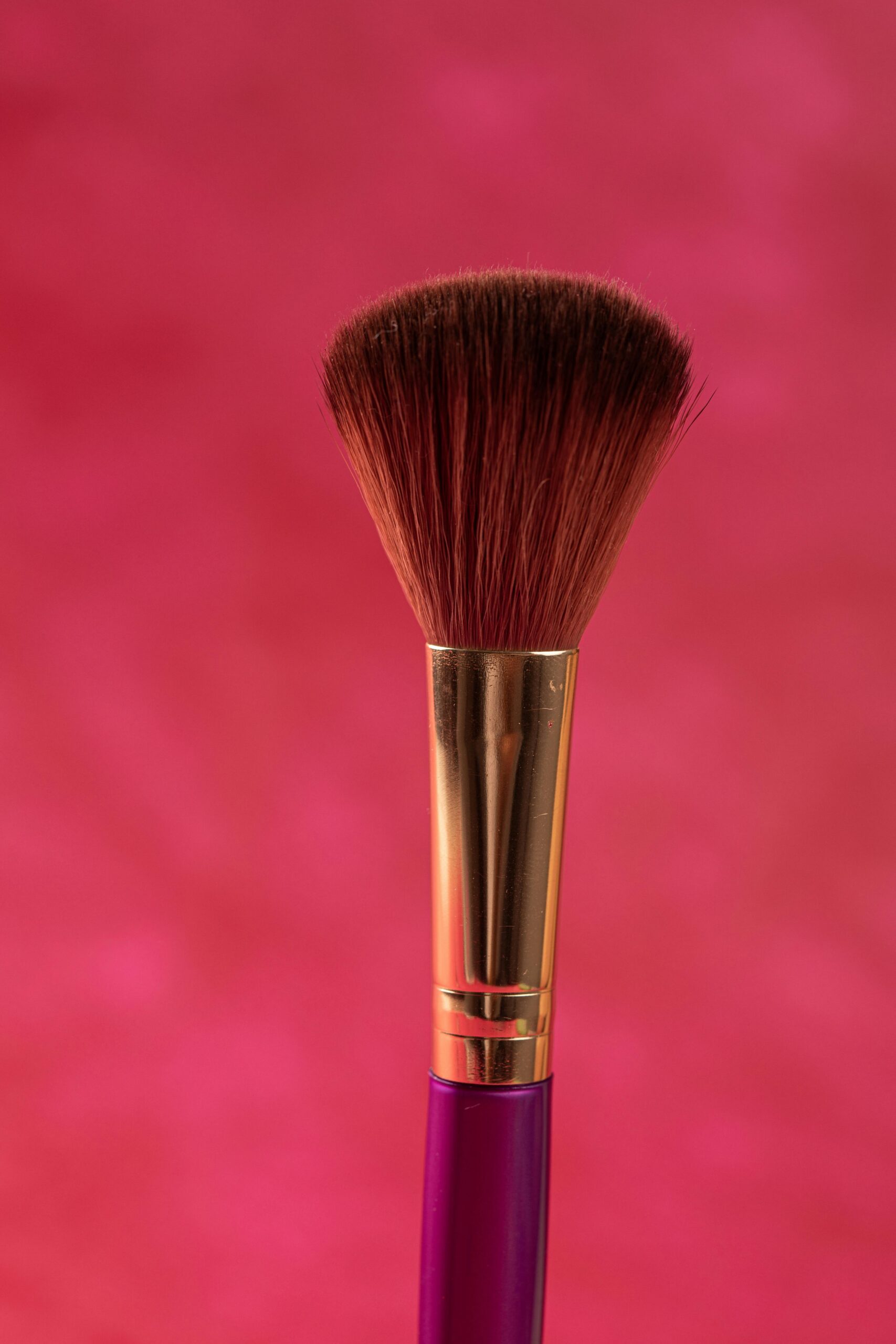 Detailed close-up of a makeup brush on a vibrant pink background, perfect for beauty and cosmetics themes.